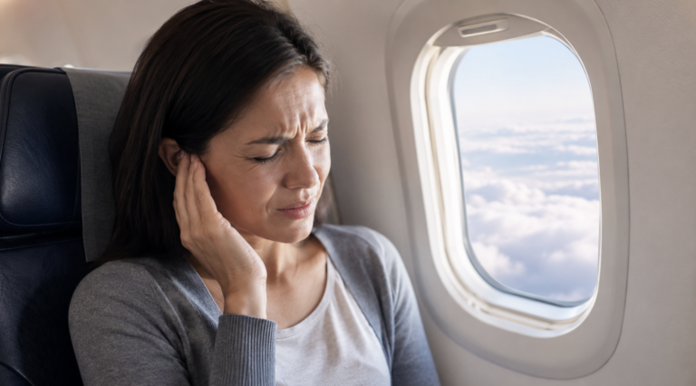 Airplane passenger pressing their ear during descent, the everyday moment when eustachian tube function equalizes cabin pressure.